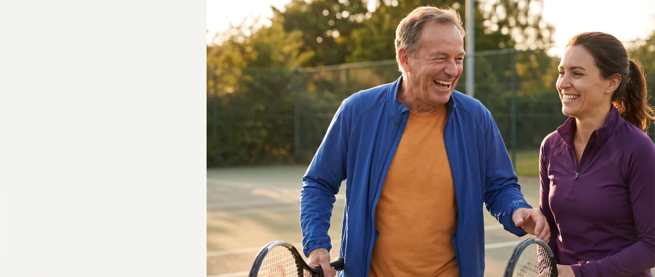 Man in his sixties laughing on a tennis court with his daughter
